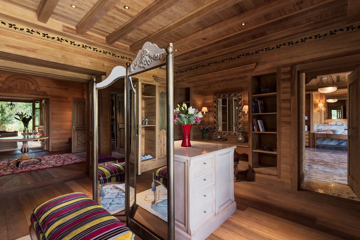A spacious room with wooden floors, a large mirror, a white cabinet, and a striped bench.