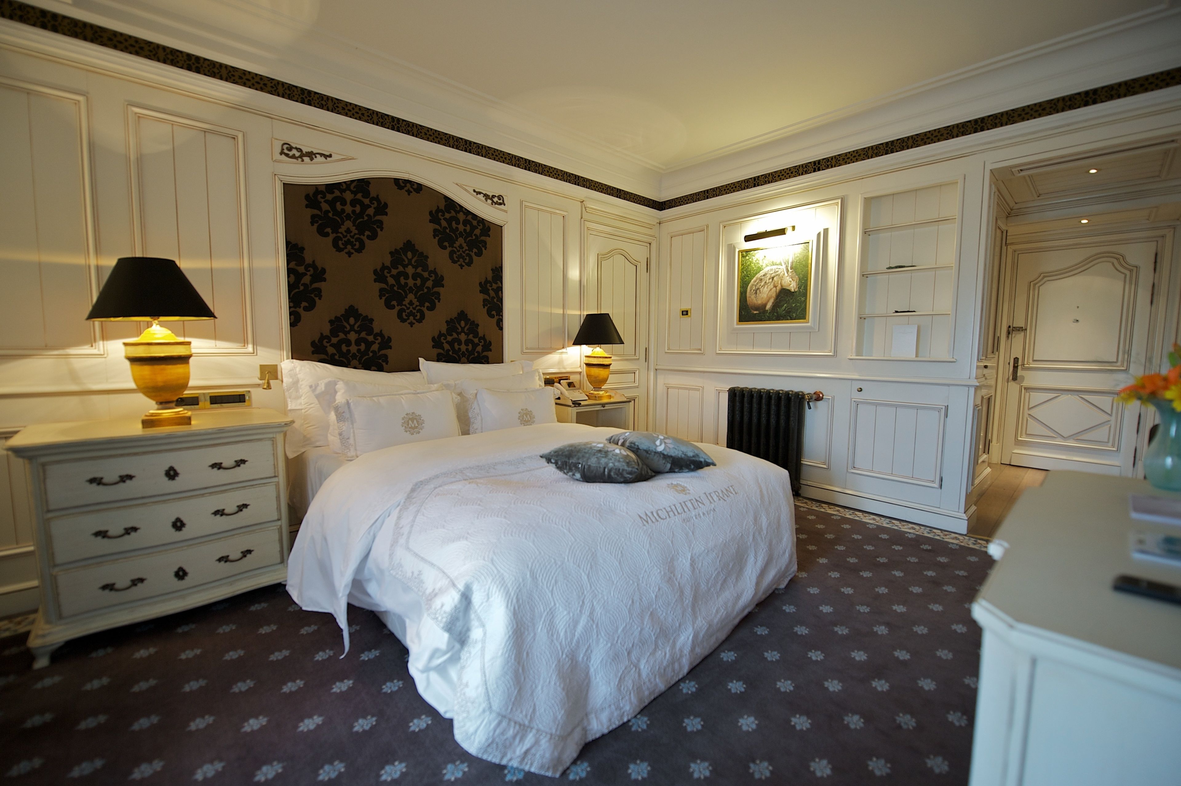 Un dormitorio con una cama grande, dos mesitas de noche con lámparas, un aparador y un radiador.
