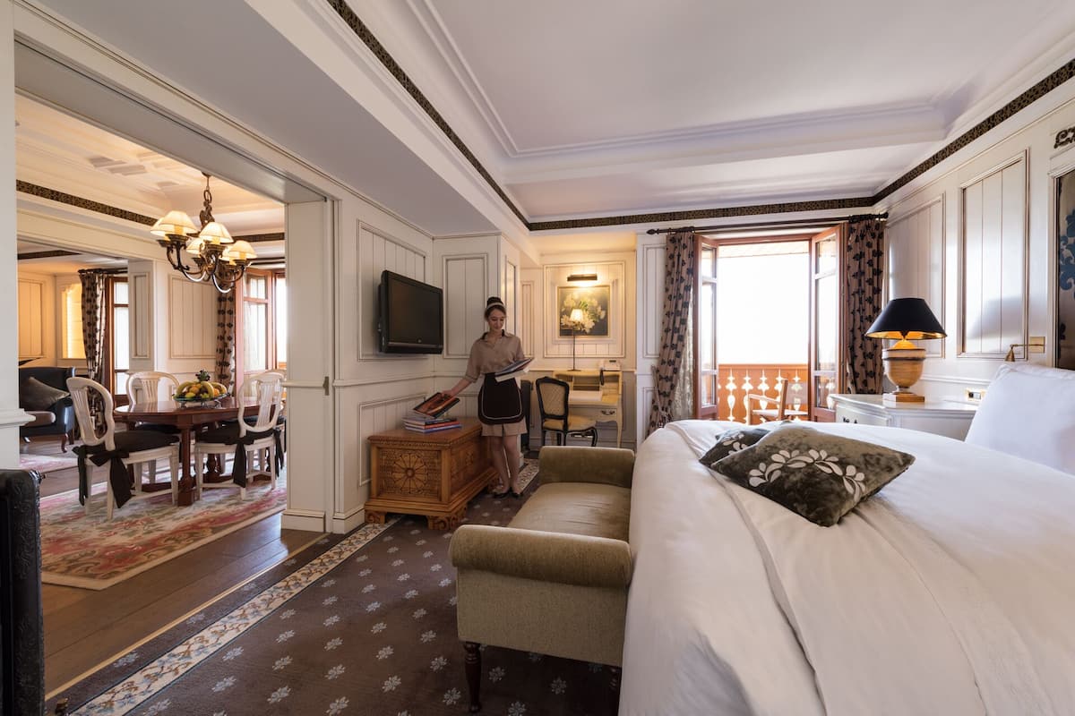 A hotel room with a bed, a desk, a television, and a dining area with chairs and a table.