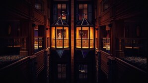 A grand hallway with ornate wooden doors and a reflective floor, leading to a central area with two illuminated lanterns.