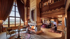 A spacious room with a fireplace, wooden furniture, and a large window offering a view.