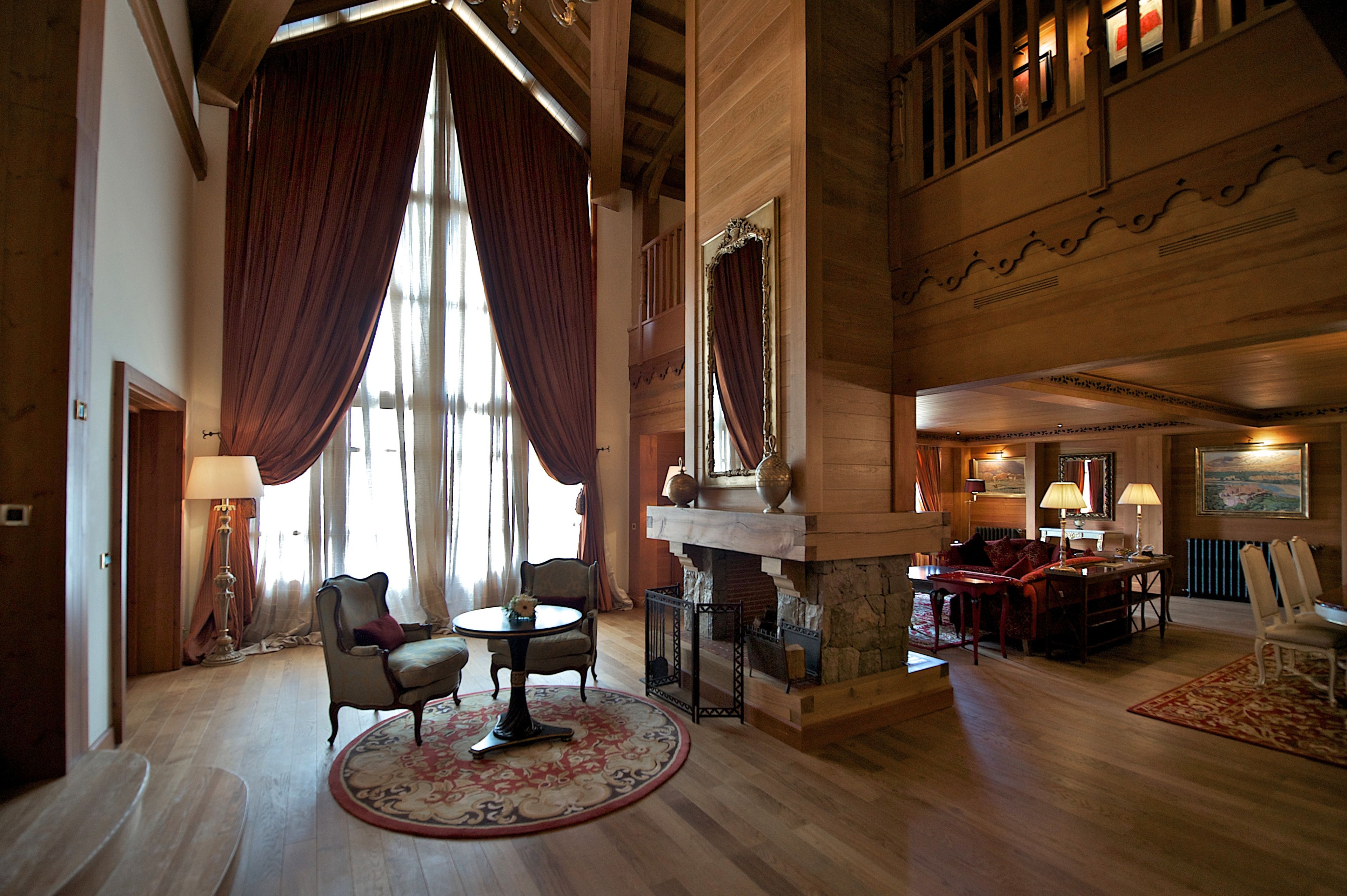A spacious lobby with a fireplace, large windows with curtains, and a high ceiling.