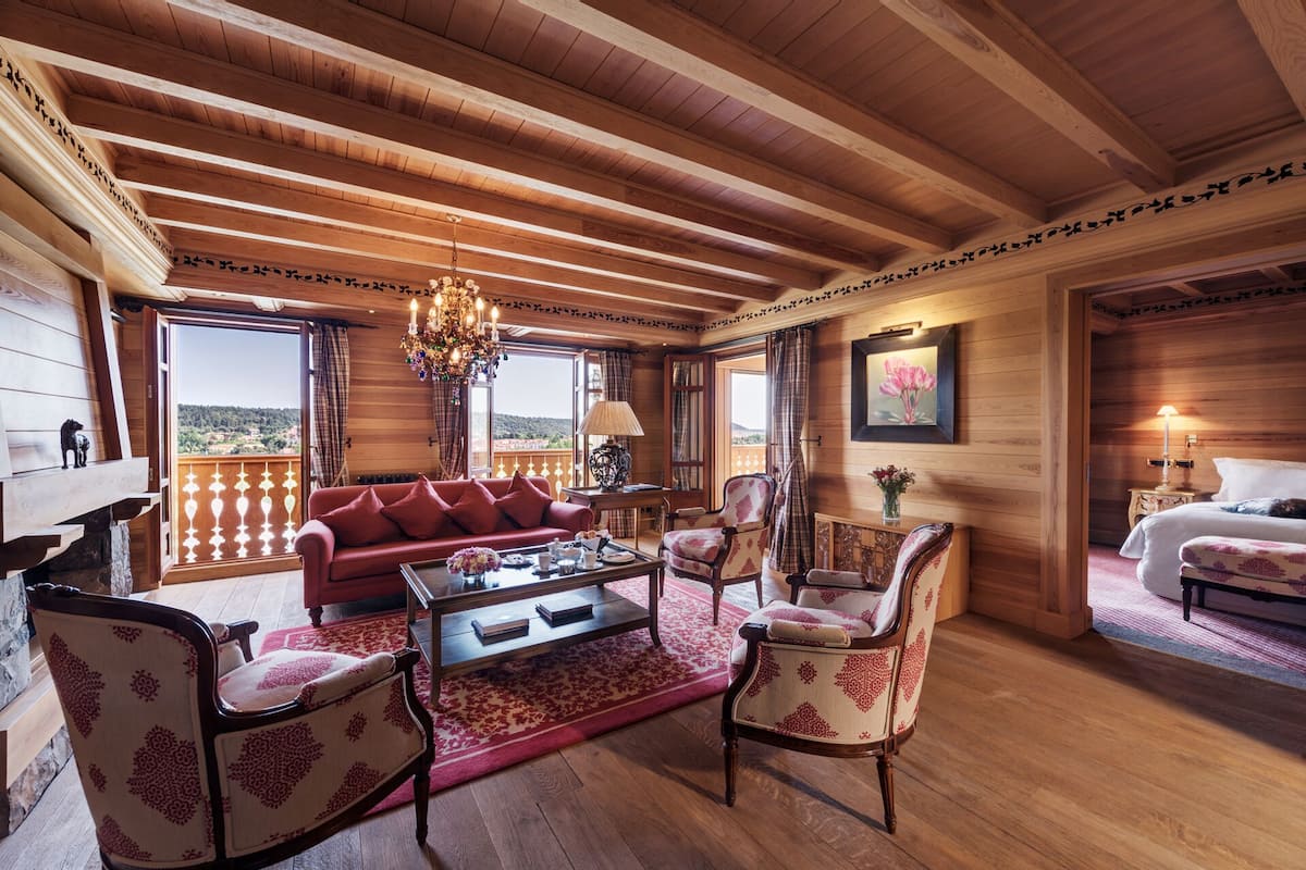 A cozy room with a wooden ceiling, a red sofa, patterned chairs, a coffee table, and a painting on the wall.