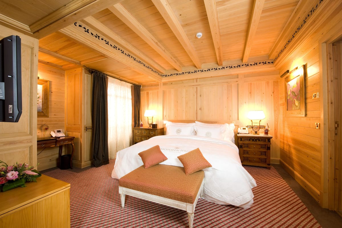 A wooden-paneled room with a large bed, bedside tables, a desk, and a bench.