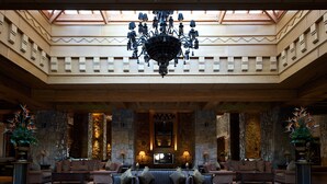 A grand lobby with a chandelier, stone walls, and a central seating area.