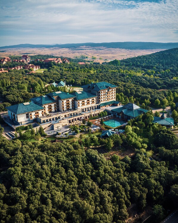 A large hotel with multiple buildings, surrounded by dense forest and hills in the background.