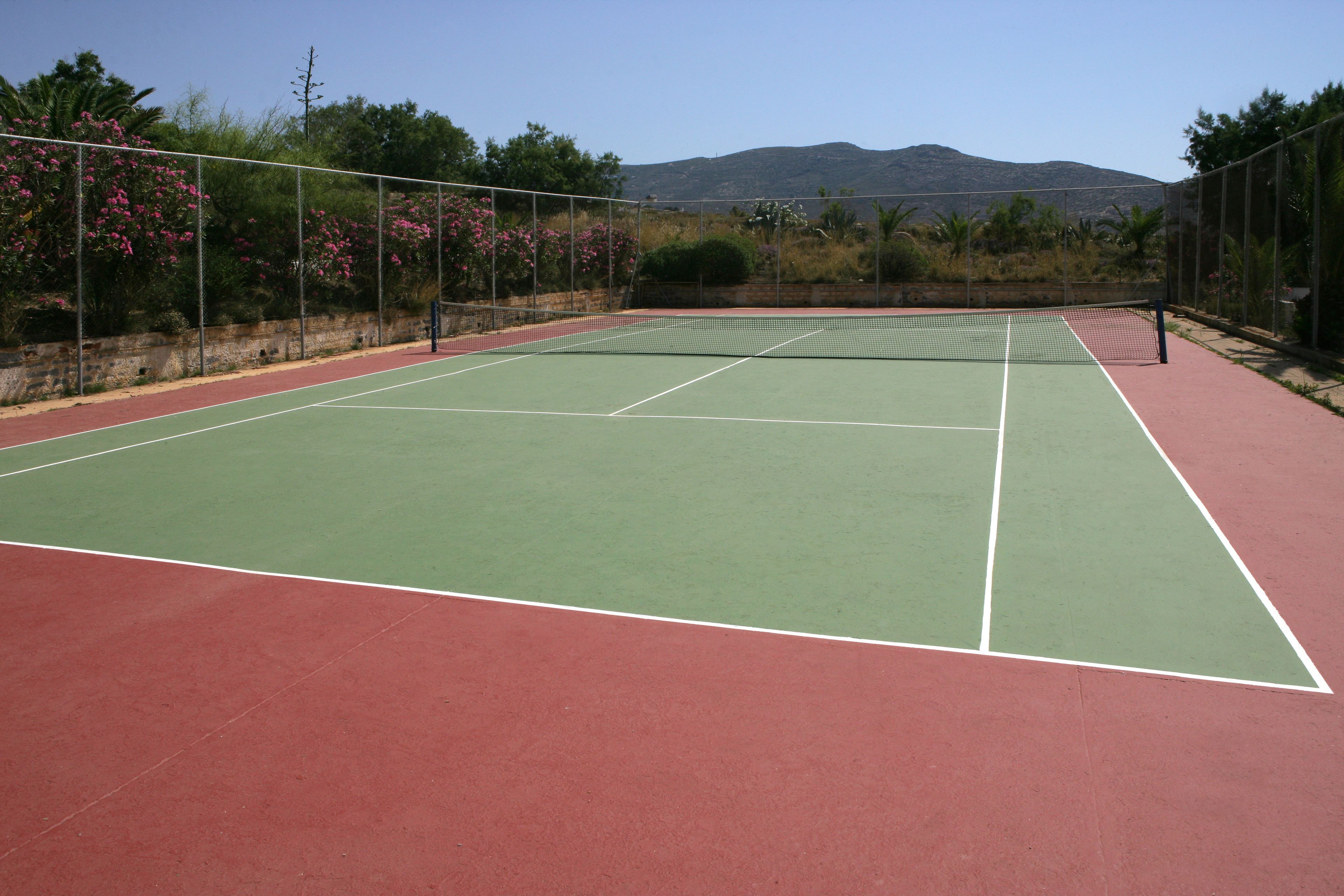 A tennis court with a net, surrounded by a fence and trees.