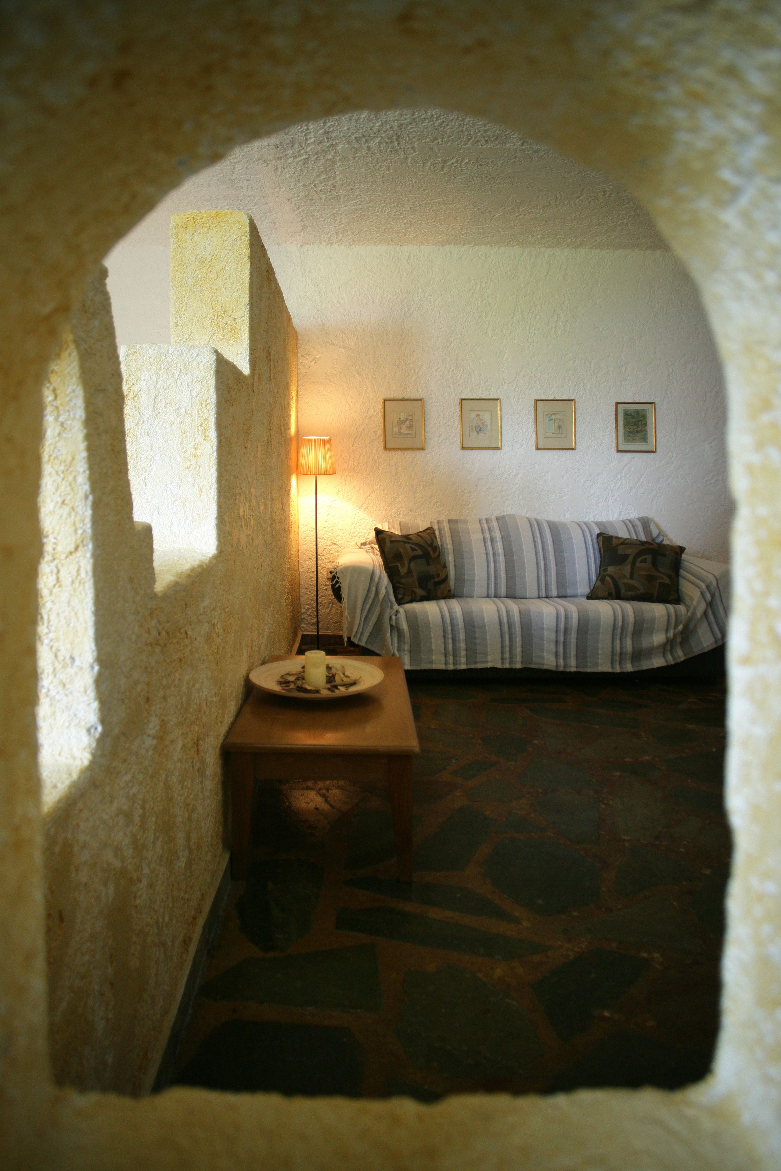 Una habitación acogedora con suelo de piedra, un sofá con cojines a rayas, una mesita con una vela y cuadros enmarcados en la pared.