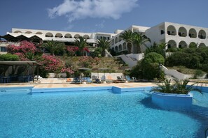 Un espace piscine avec une eau d’un bleu limpide, des chaises longues et un bâtiment doté de fenêtres en arc de cercle et de balcons.