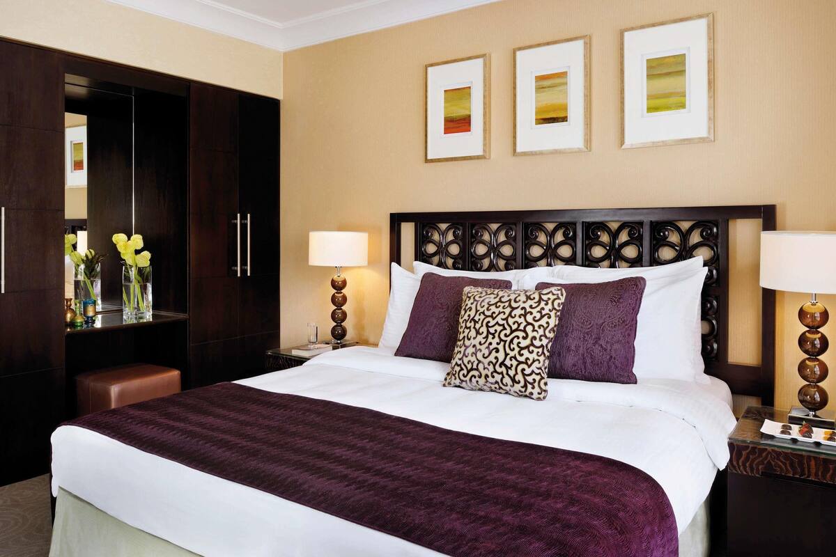 A hotel room with a large bed, two bedside tables, a wardrobe, and three framed pictures on the wall.