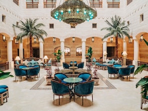 A spacious lobby with high ceilings, ornate chandeliers, and a central seating area with tables and chairs. - Mövenpick Resort Petra (Wadi Musa)