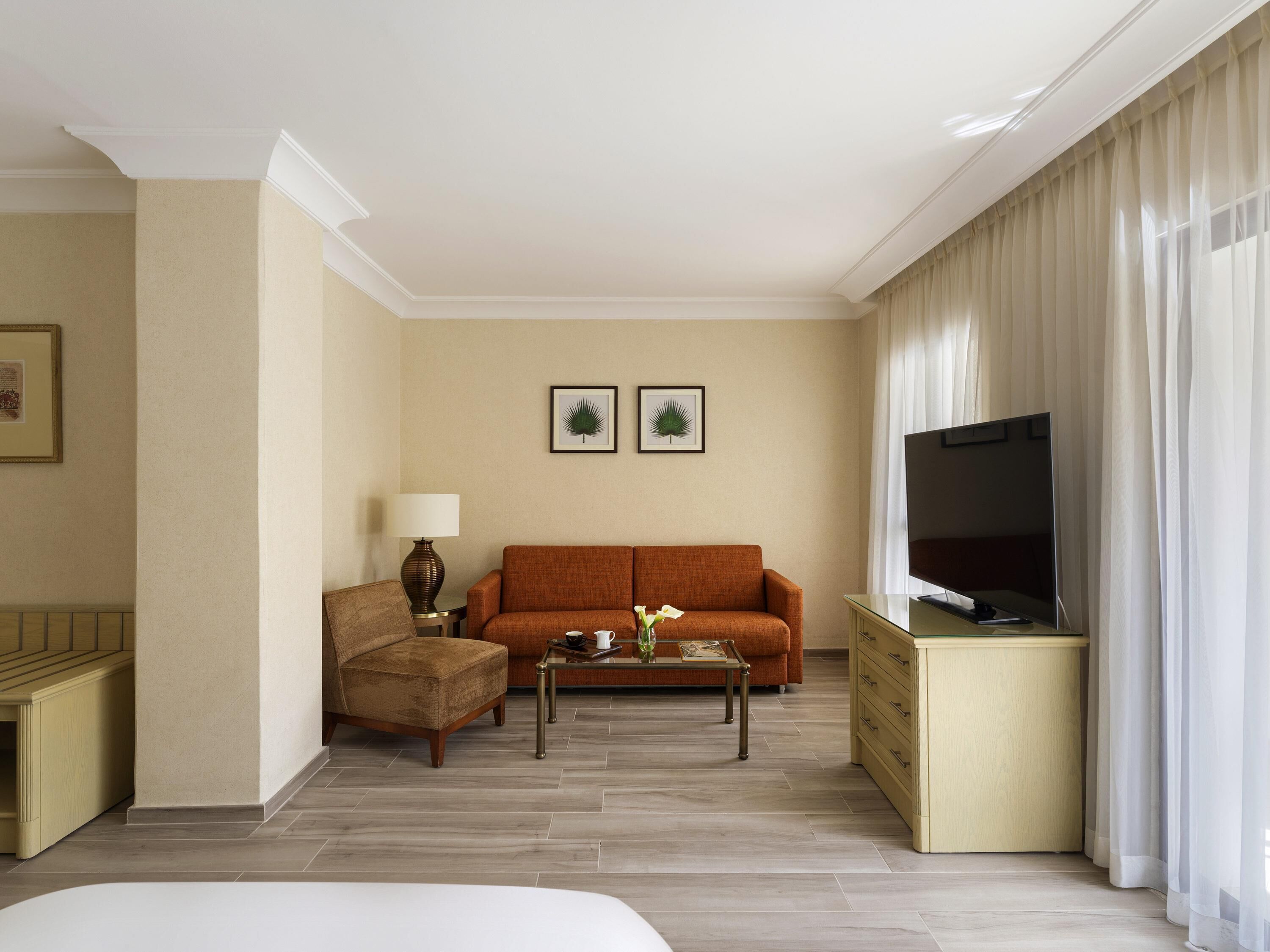 A hotel room with a sofa, a coffee table, a TV, a lamp, and a bed.