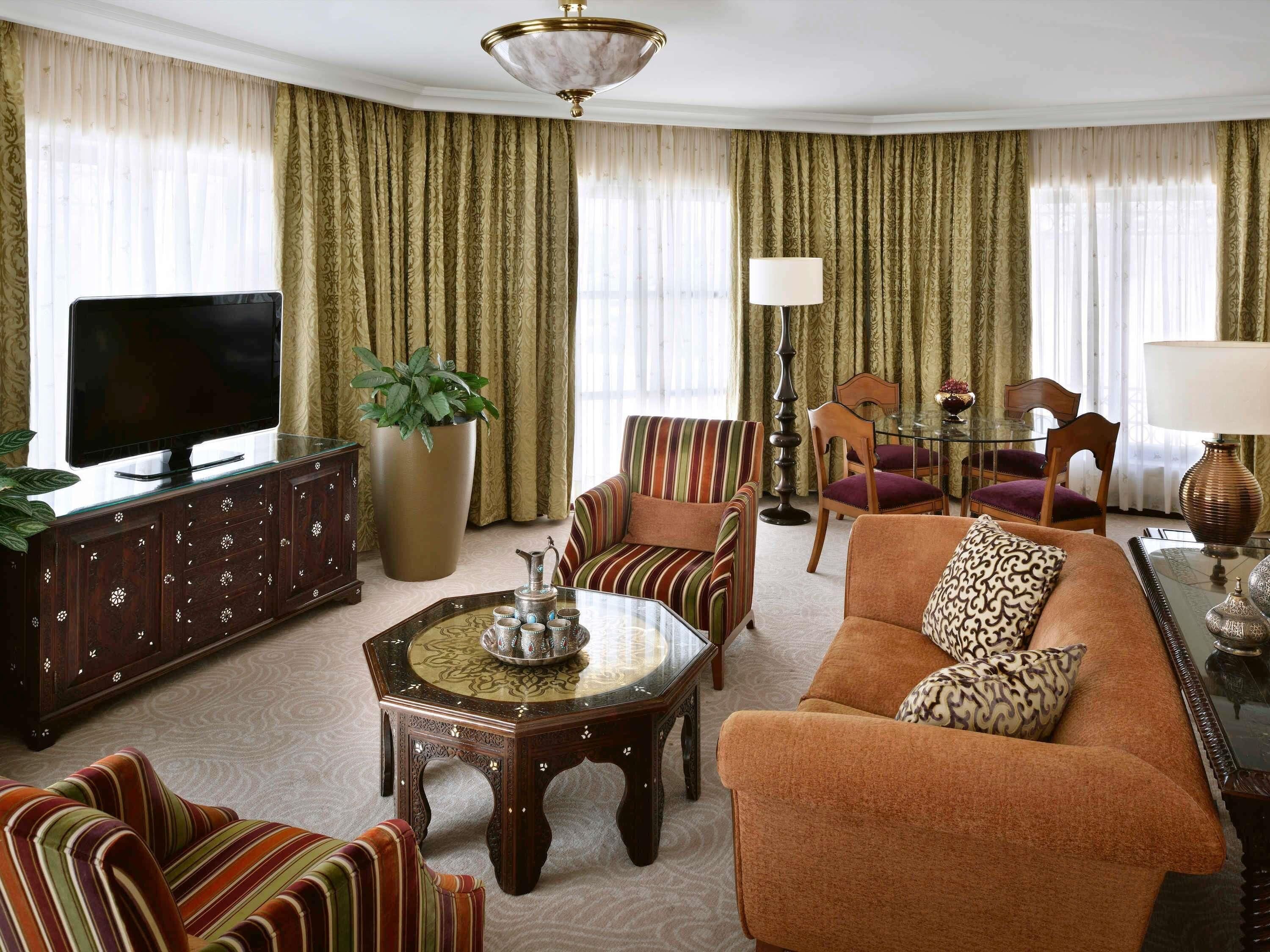 A living room with a TV, sofa, chairs, a coffee table, and curtains.