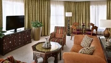 A living room with a TV, sofa, chairs, a coffee table, and curtains.