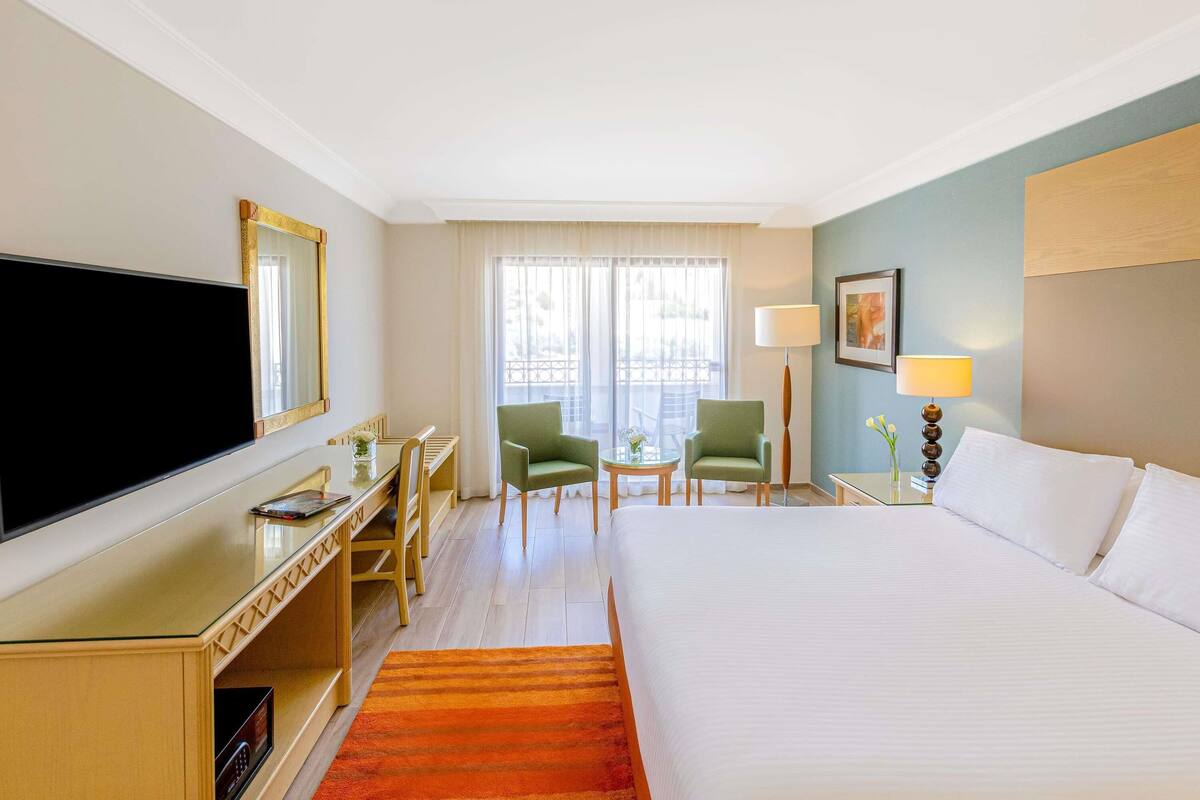 A hotel room with a bed, a desk, two chairs, a television, and a window with curtains.