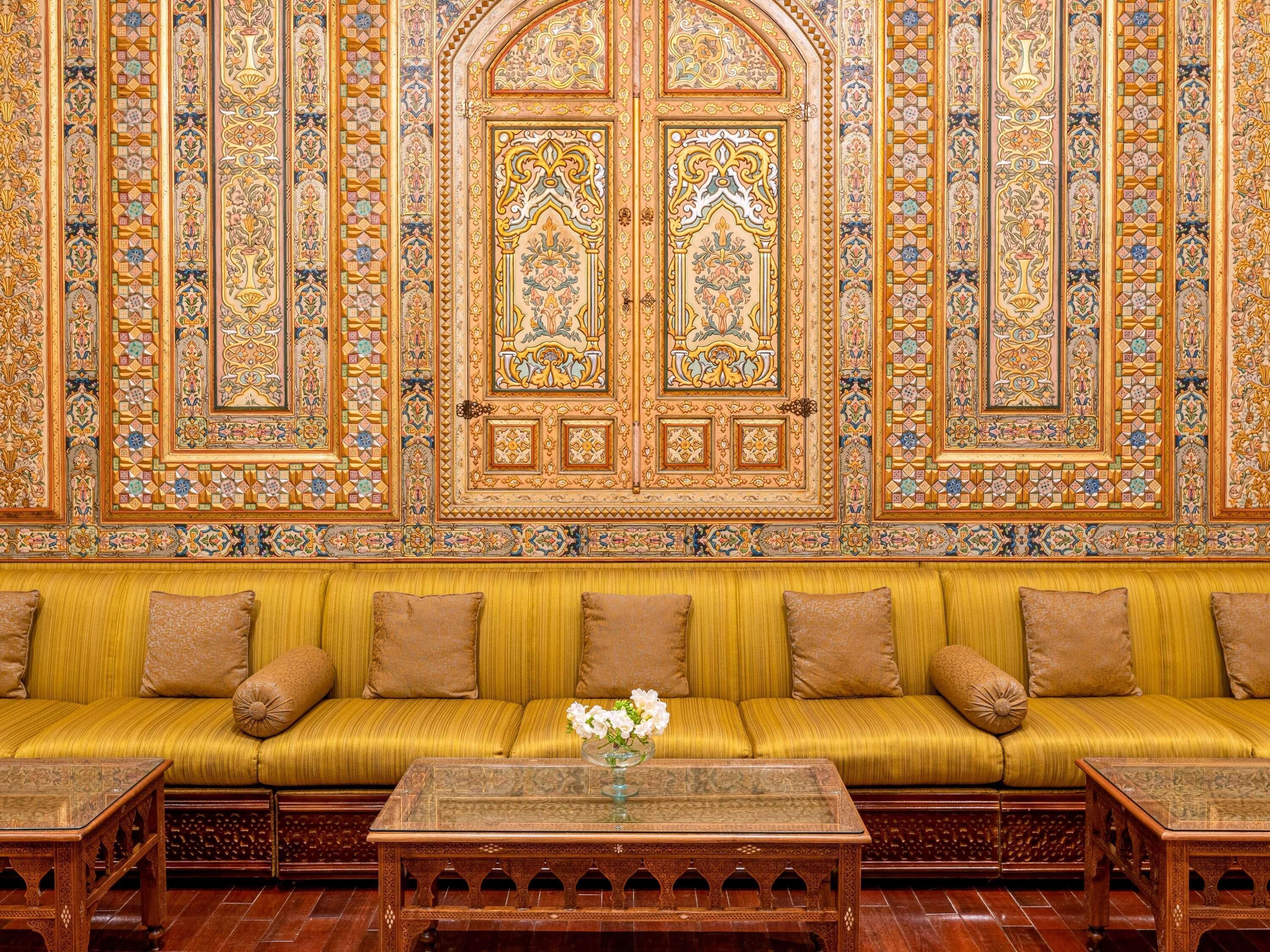 A room with a sofa set against a wall with intricate tile work and a large arched doorway.