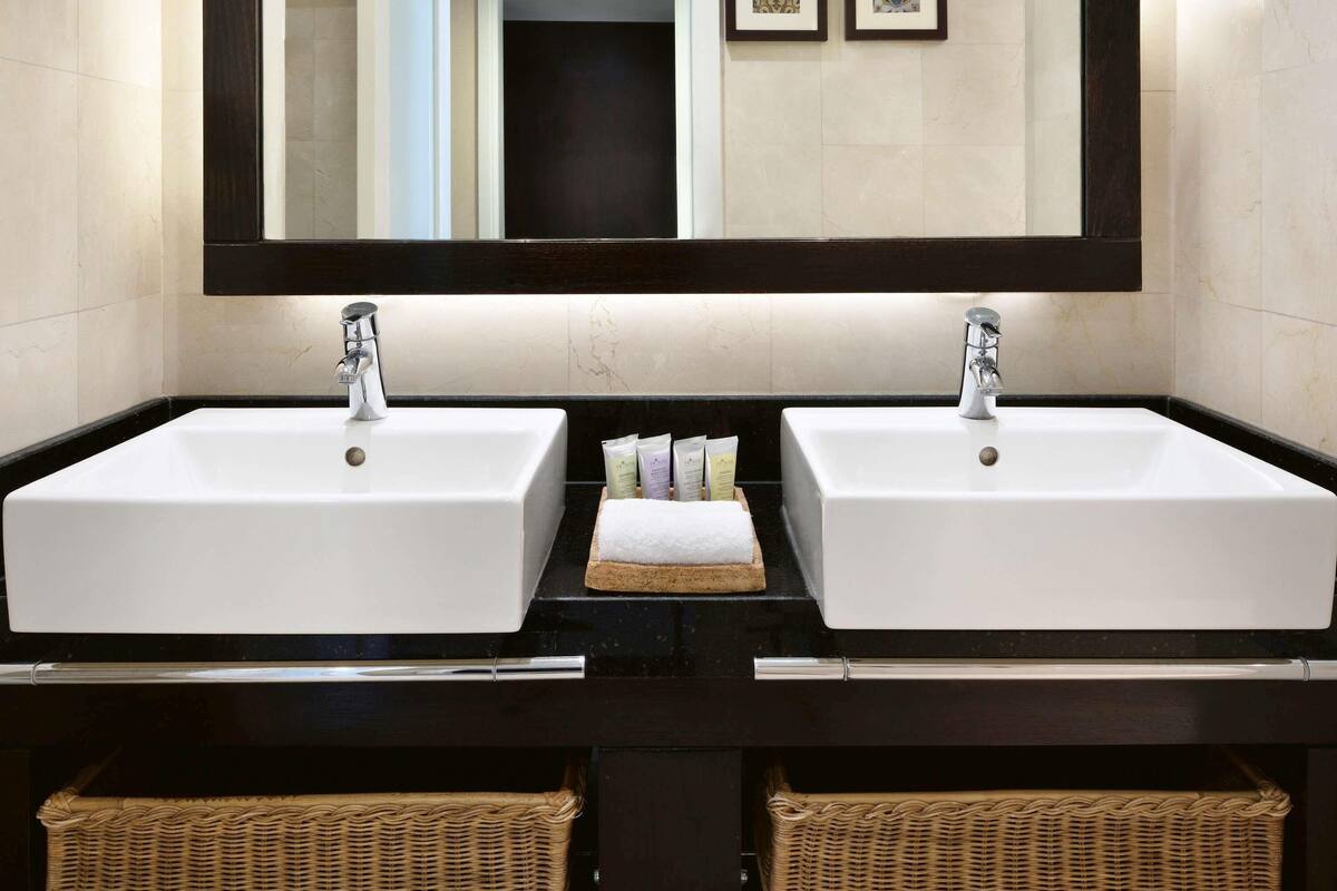 A bathroom with two white sinks, a large mirror, and wicker baskets under the sinks.