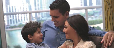 A family sitting on a couch with a city view through a large window.