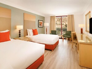 A hotel room with two beds, a desk, a chair, a TV, and a window with a view. - Mövenpick Resort Petra (Wadi Musa)