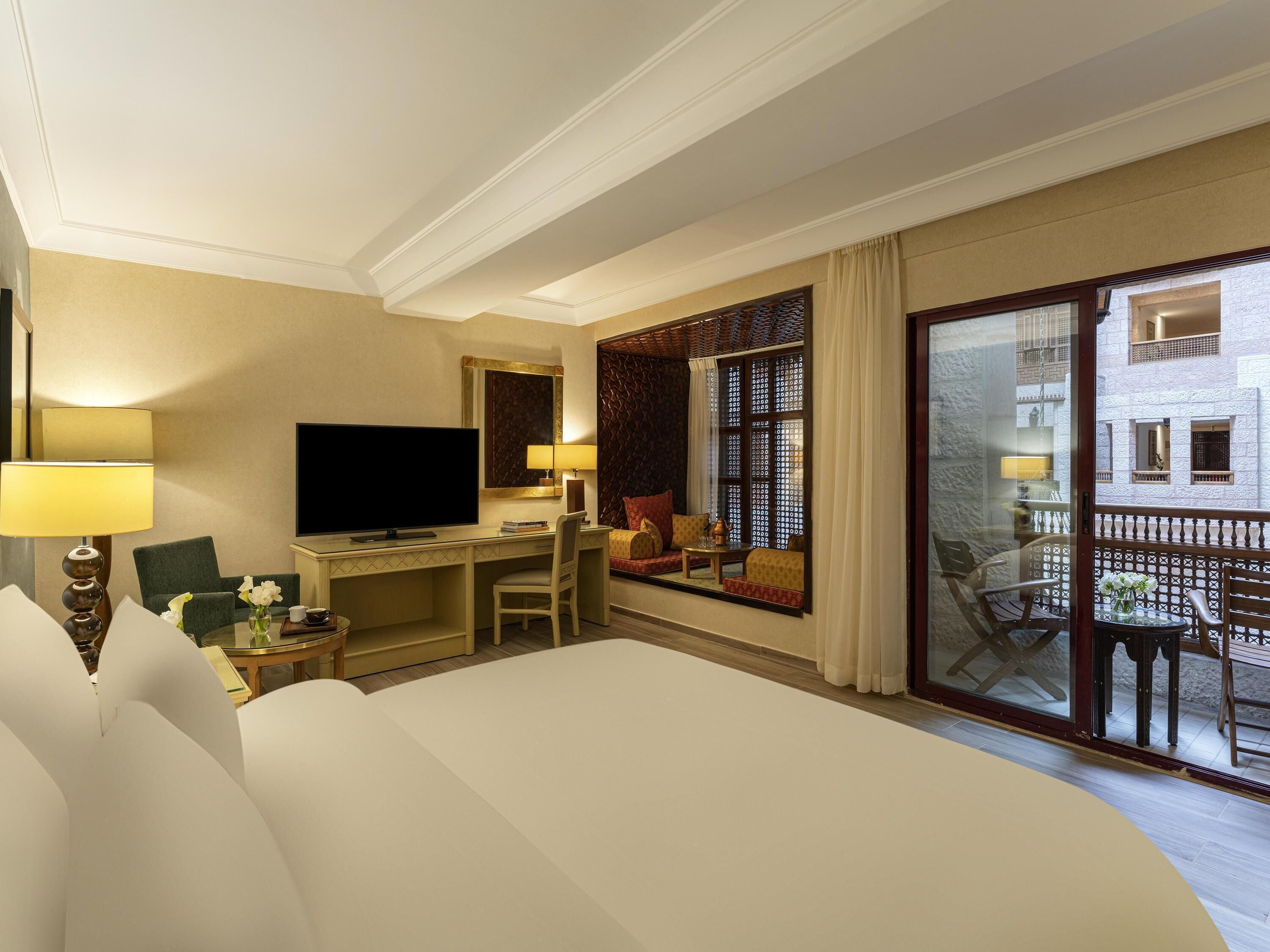 Una habitación de hotel con cama, escritorio, televisión y balcón con vistas.