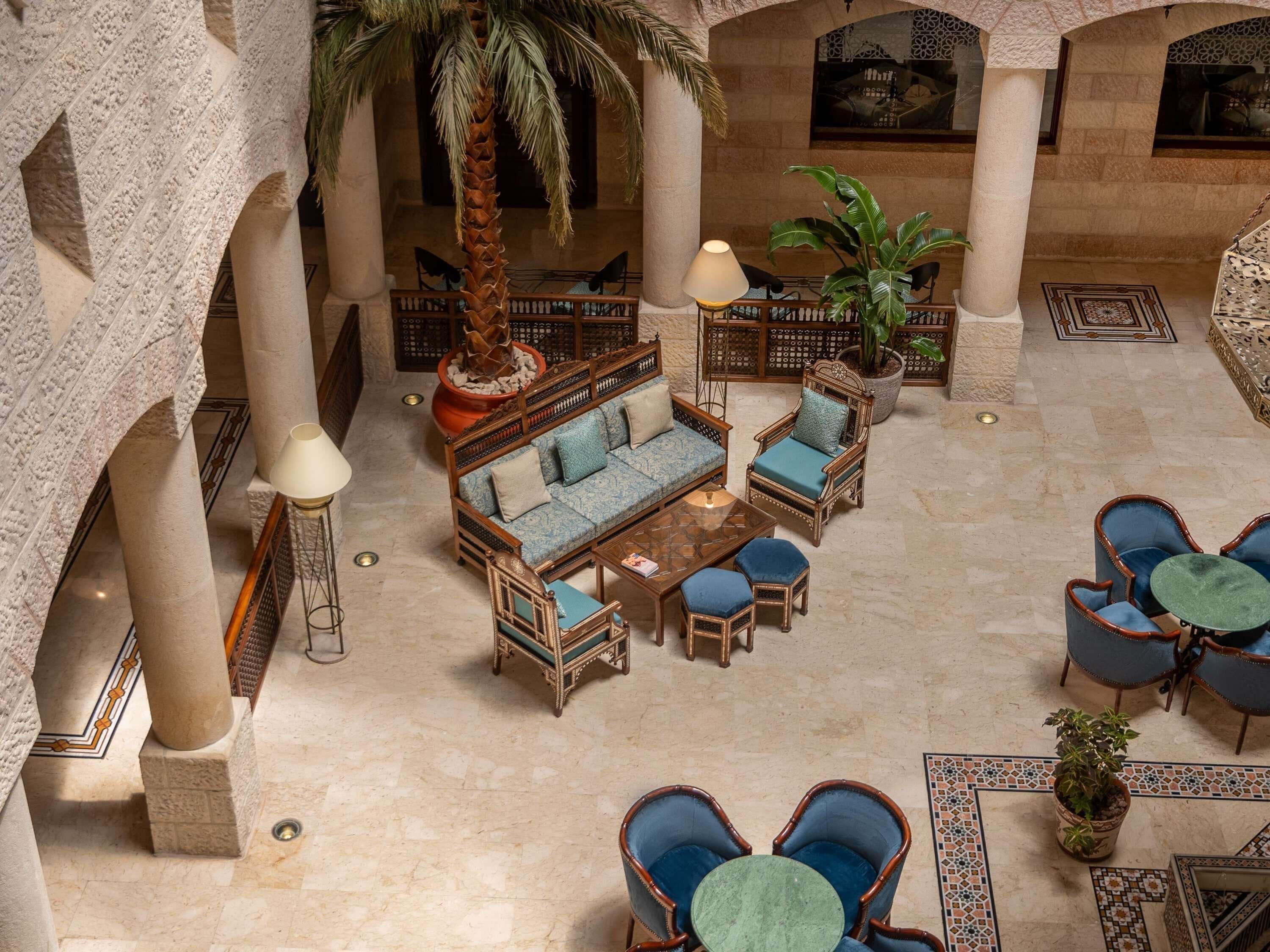 A spacious lobby with a central seating area, palm trees, and a decorative fountain.