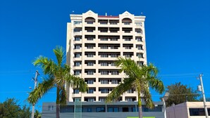 A multi-story hotel with a symmetrical facade, balconies on each floor, and palm trees in front. - Aquarius Beach Tower (Saipan)