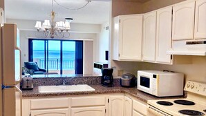 A kitchen with white cabinets, a granite countertop, a built-in oven, a microwave, a coffee maker, and a toaster. - Aquarius Beach Tower (Saipan)