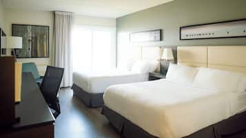 A hotel room with two beds, a desk, a chair, a lamp, and a painting on the wall.