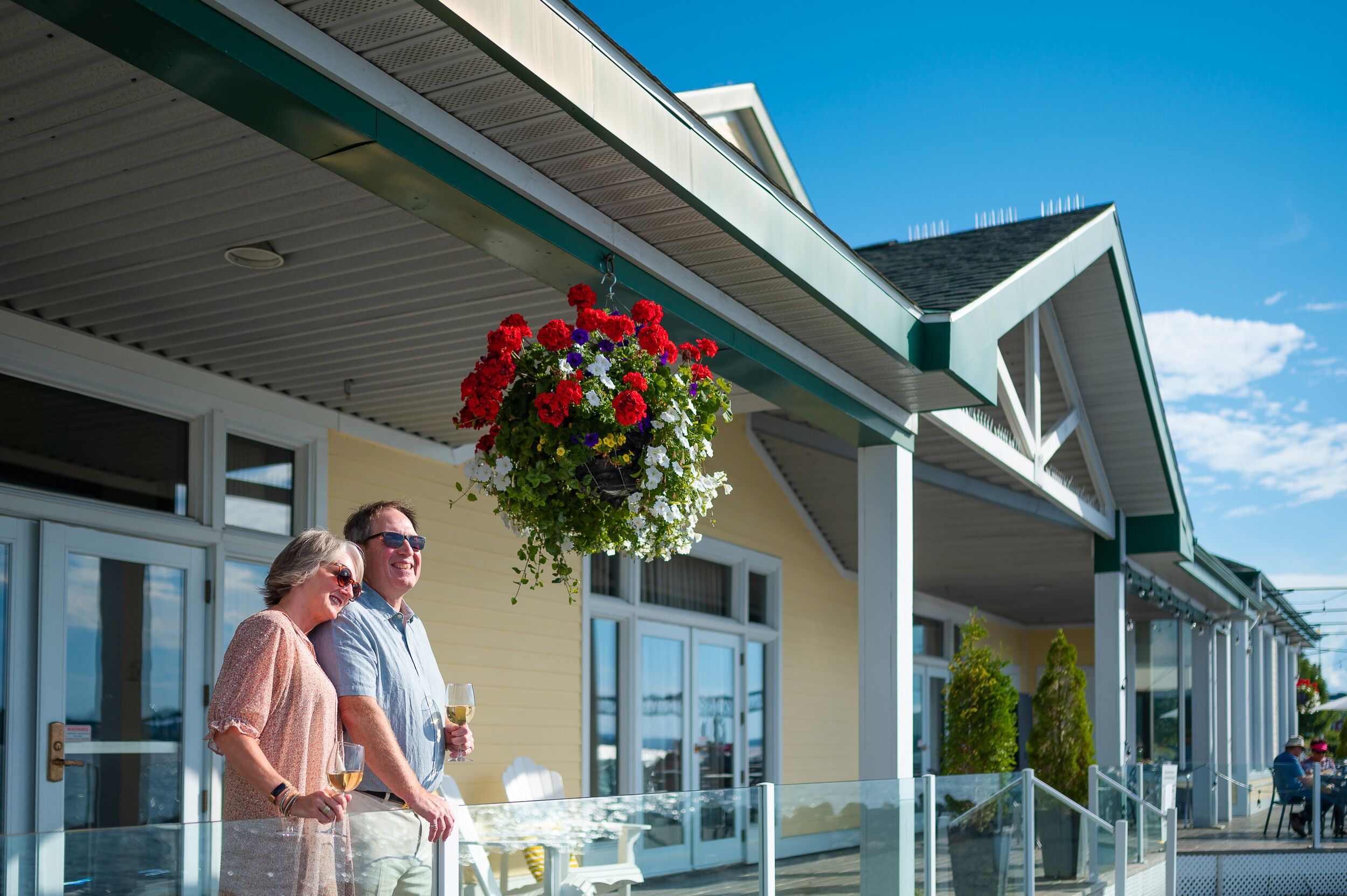 A building with a covered patio area, outdoor seating, and a hanging flower basket.