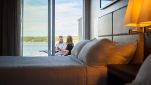 A hotel room with a large window offering a view of the water and greenery. - Rodd Miramichi (Miramichi)