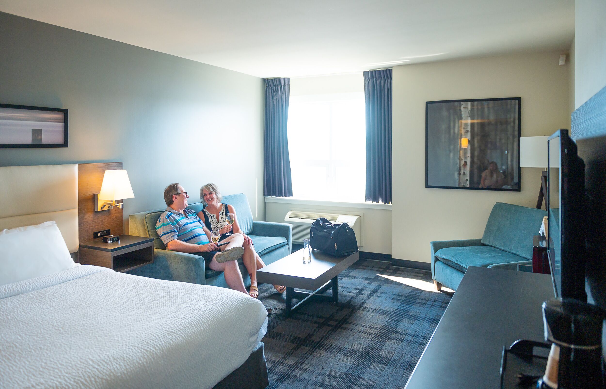 A hotel room with a bed, two sofas, a coffee table, and a TV.