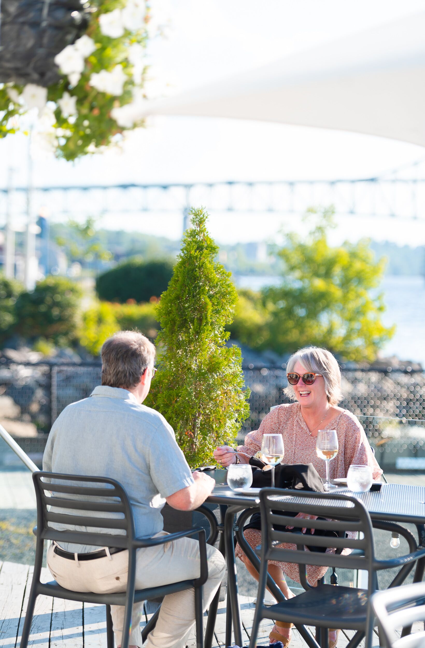 A couple dining at an outdoor table with a view of a bridge and greenery.