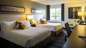 A hotel room with two beds, a desk, and a chair. There are lamps on the bedside tables and a window with curtains.