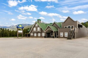 A Days Inn with a green roof, a stone facade, and a mountain backdrop.