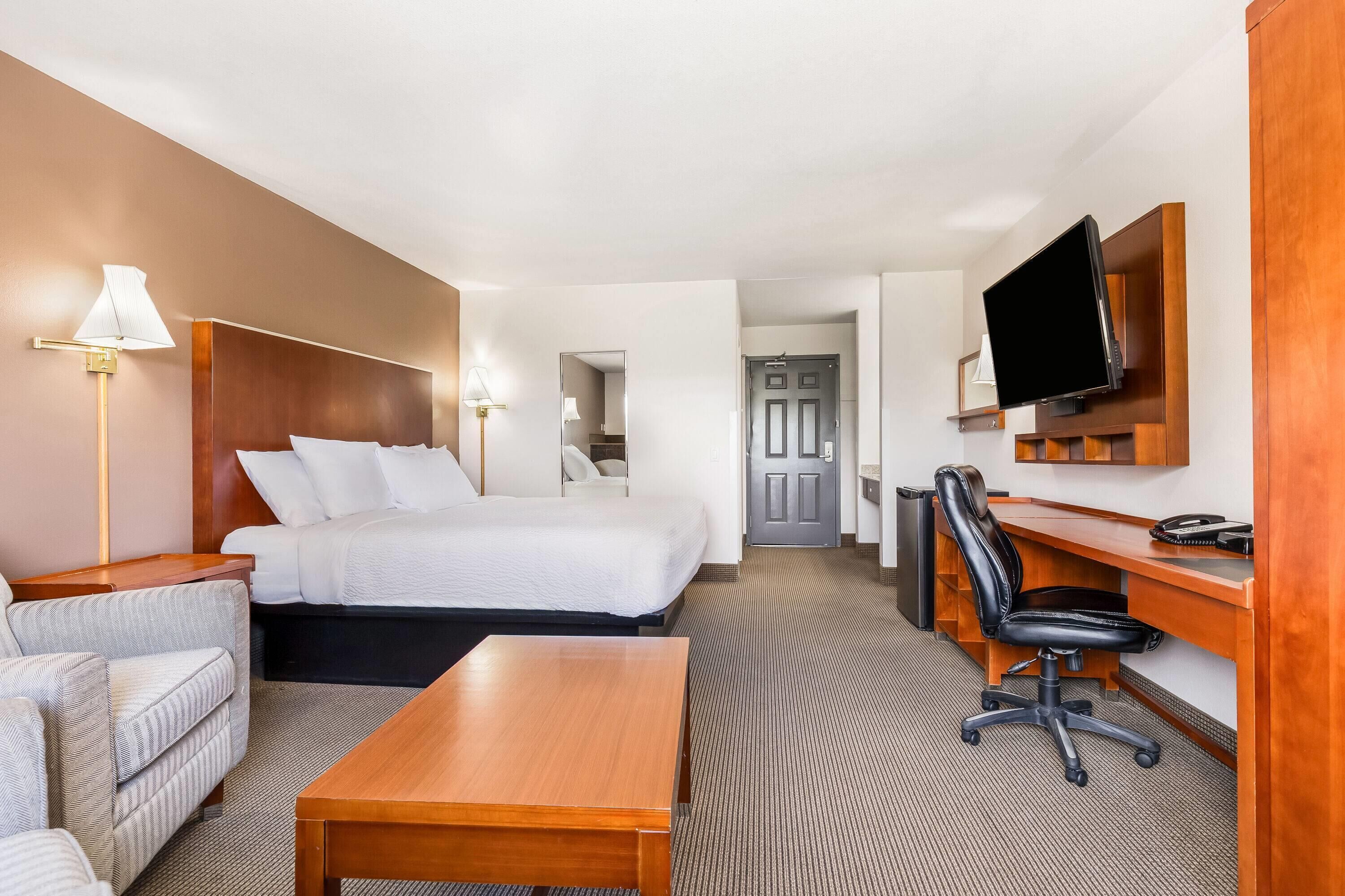 A hotel room with a bed, a desk, a chair, a TV, and a lamp.