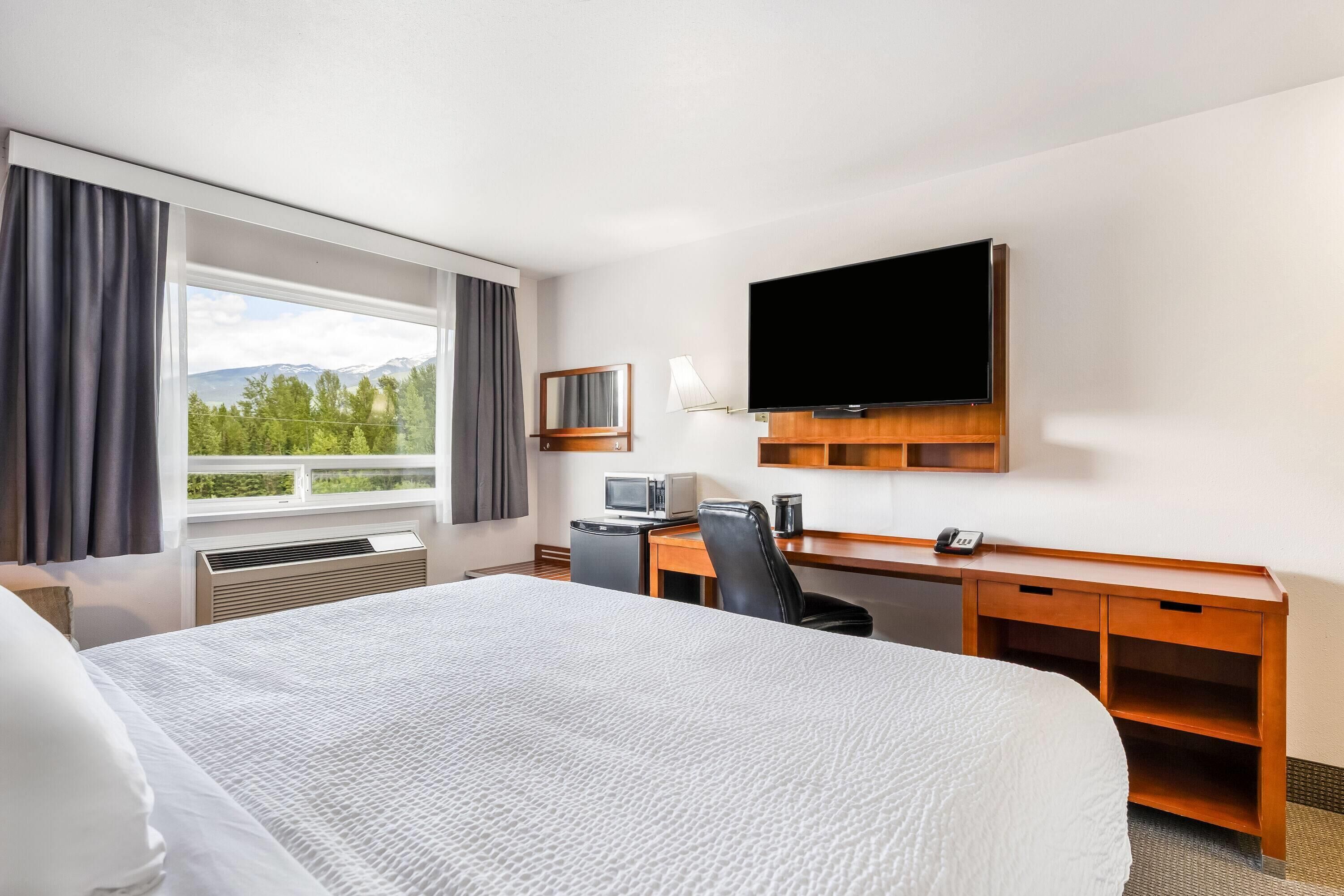A hotel room with a bed, desk, TV, and a window with a view.
