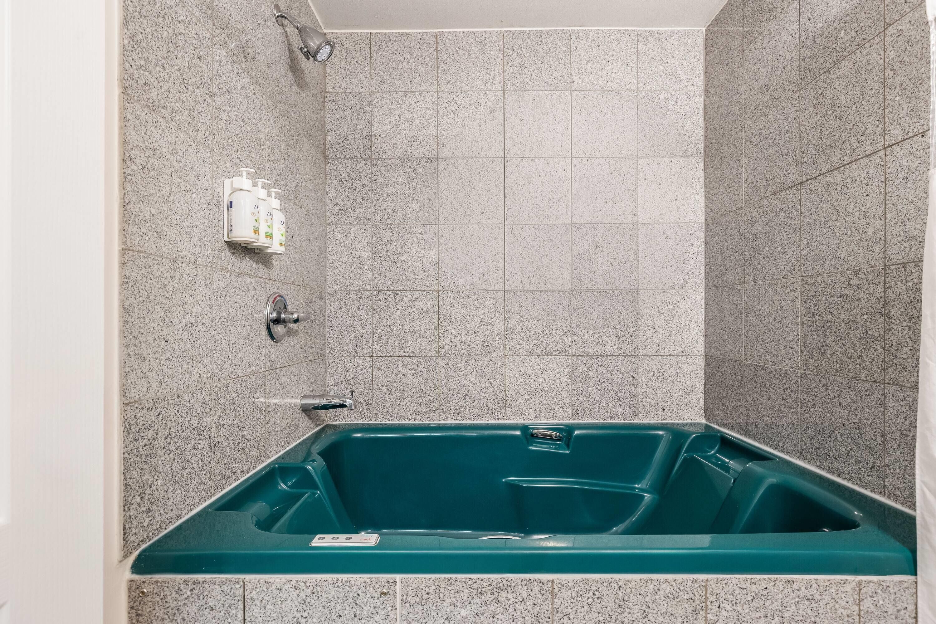 A bathroom with a bathtub, a showerhead, and a wall-mounted soap dispenser.