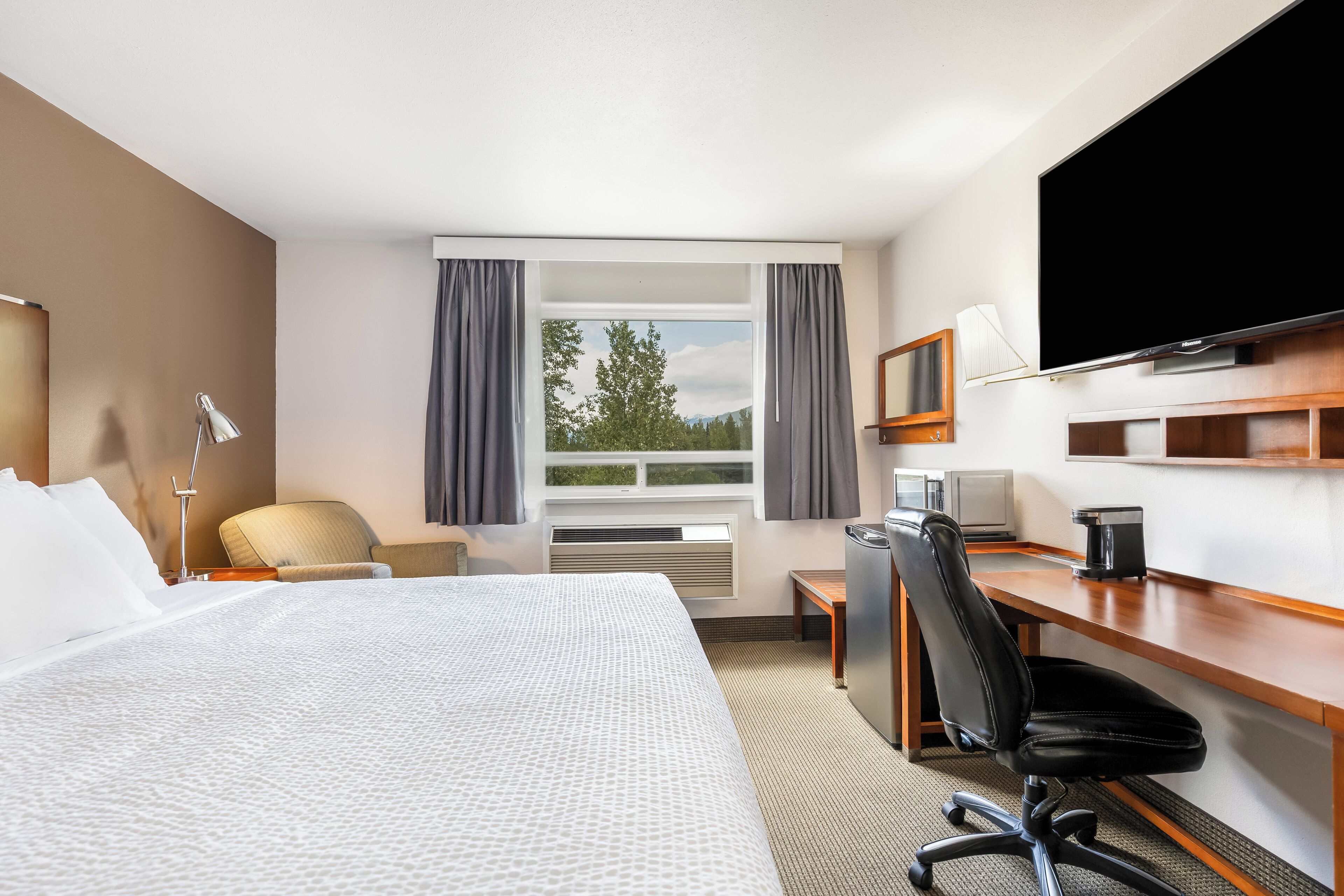 Ein Hotelzimmer mit Bett, Schreibtisch, Stuhl, Fernseher und einem Fenster mit Vorhängen.