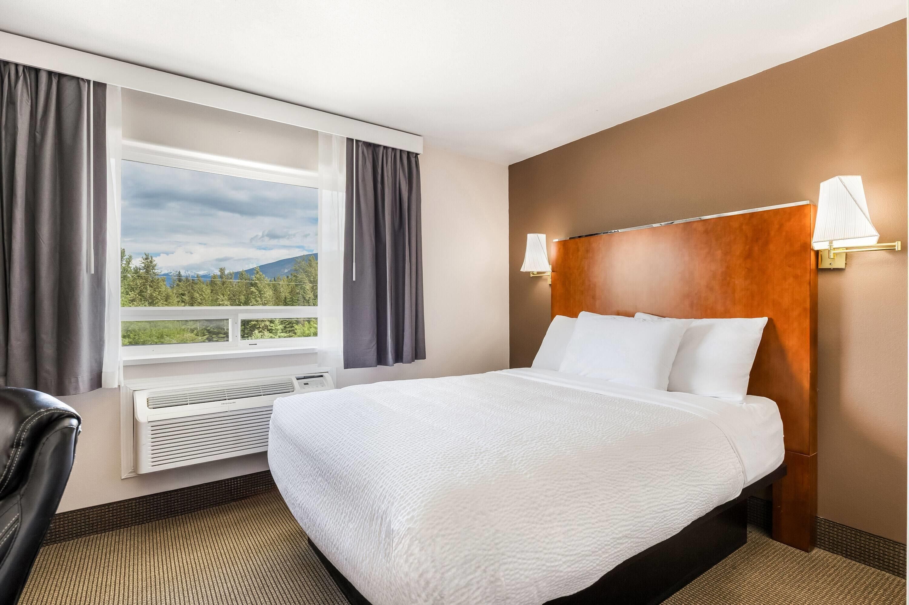 Hotellihuone, jossa on suuri sänky, ikkuna, jossa on verhot, seinään kiinnitetty valaisin sekä näkymä vehreään maisemaan ja vuorille.