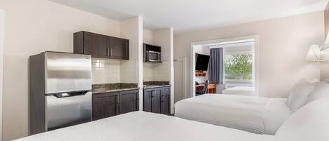 A hotel room with a kitchenette, two beds, a TV, and a window with a view.