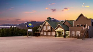 A Days Inn with a two-story structure, a covered parking area, and a mountainous backdrop. - Days Inn by Wyndham Valemount (Valemount)