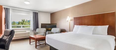 A hotel room with a large bed, a desk, a chair, a lamp, and a view of greenery through the window.