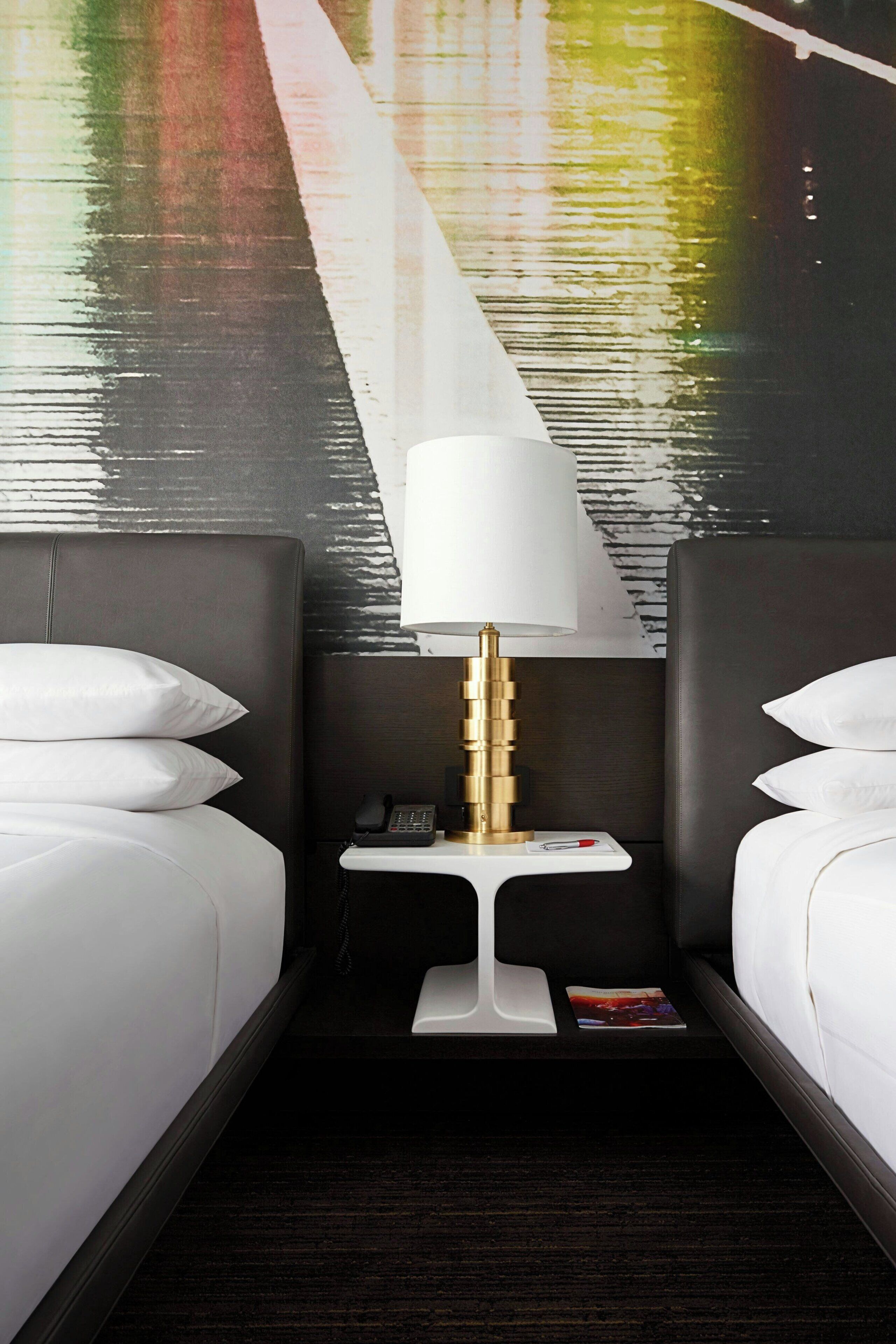 A hotel room with two beds, a nightstand with a lamp, and a wall mural.