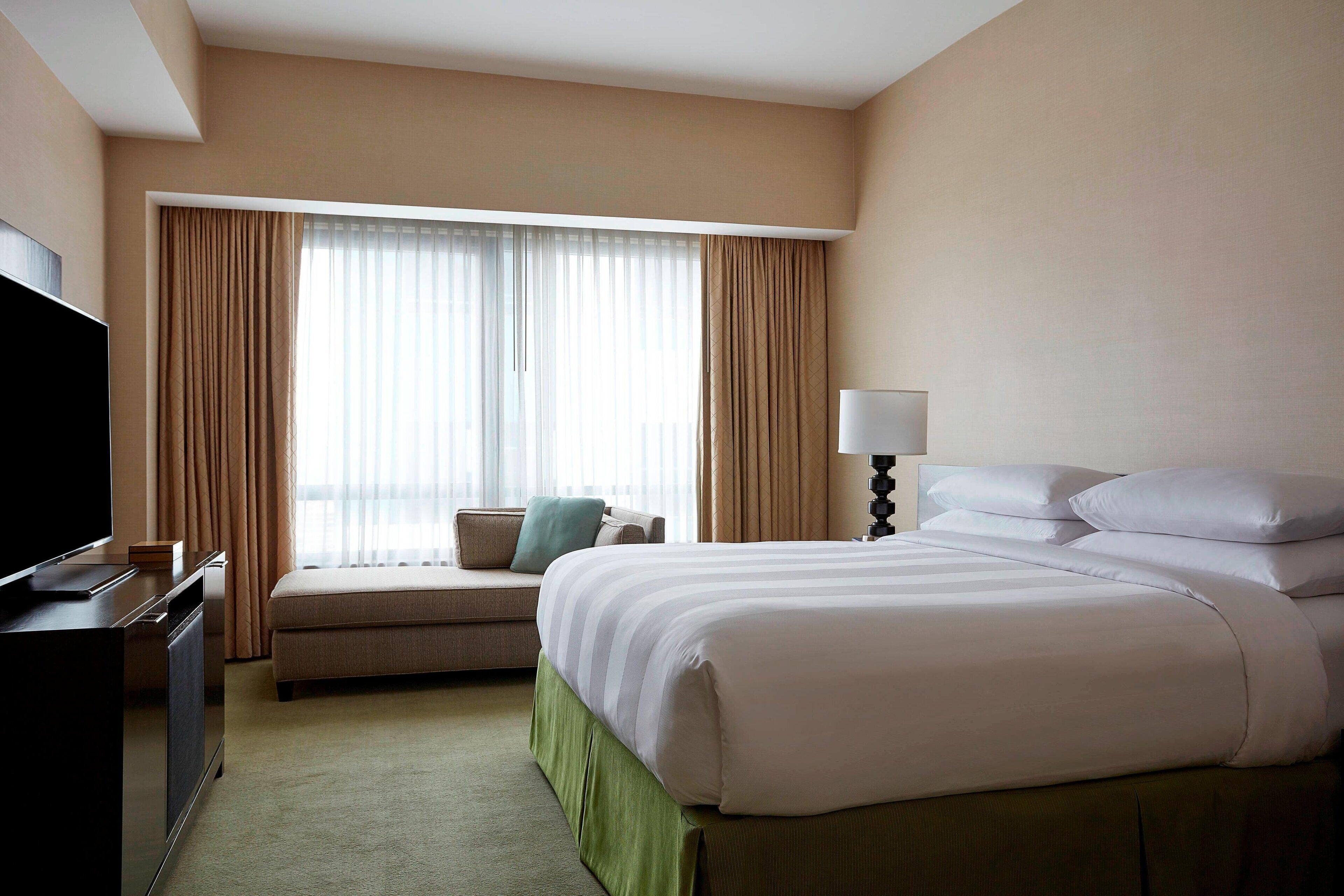 A hotel room with a large bed, a TV, a sofa, and a window with curtains.
