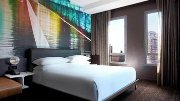 A hotel room with a large bed, a nightstand, a telephone, a window with curtains, and a cityscape view.