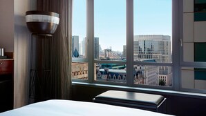 Une chambre d’hôtel dotée d’une grande fenêtre donnant sur la ville, d’une table de chevet et d’un lampadaire.