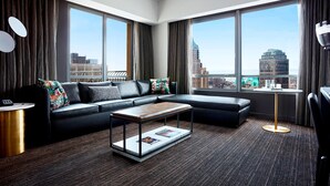 Une chambre d’hôtel moderne avec un canapé d’angle, une petite table basse et de grandes fenêtres donnant sur la ville.