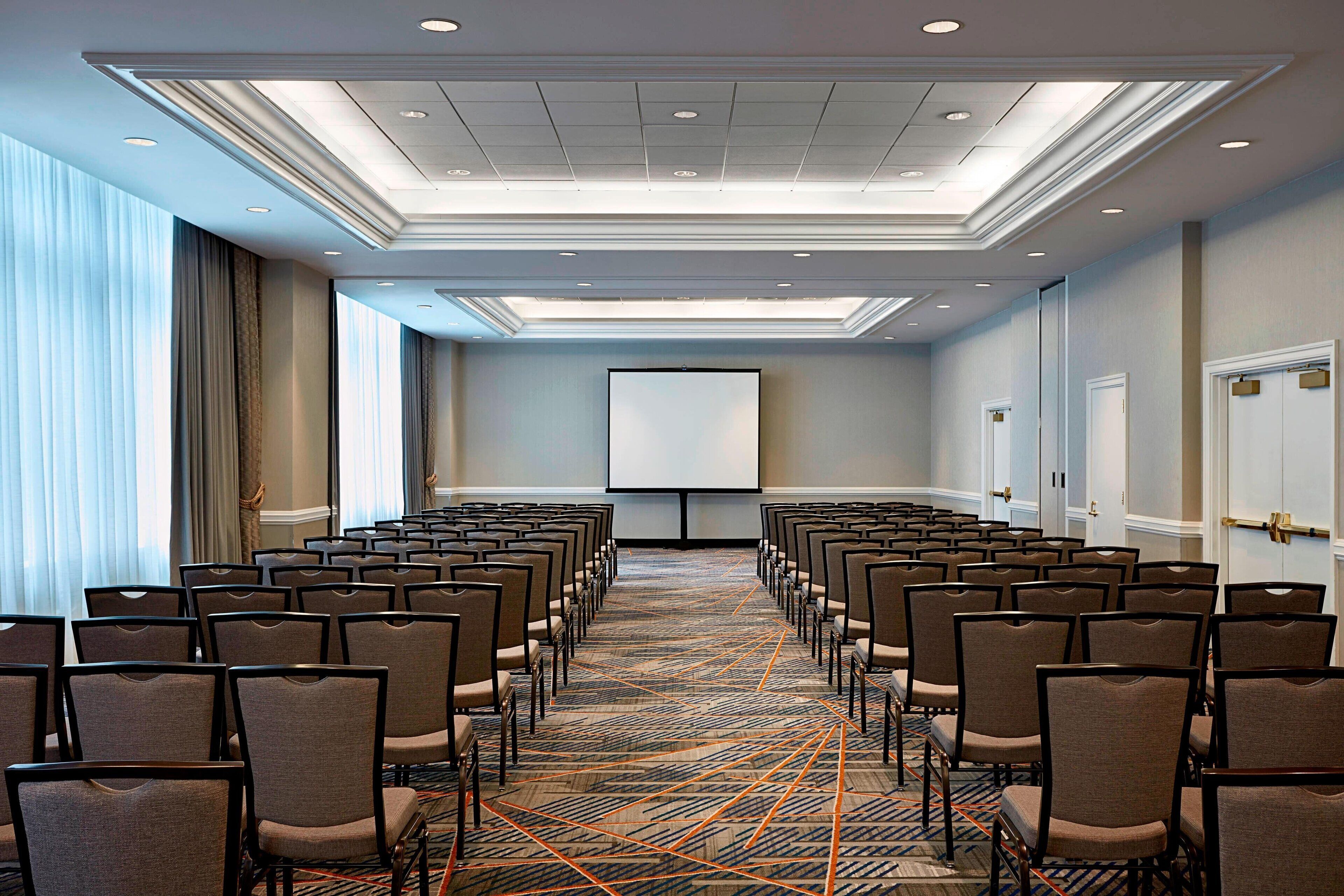 A conference room with rows of chairs, a projector screen, and a carpeted floor.
