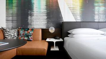 A hotel room with a bed, a small table, a chair, and a nightstand with a lamp.