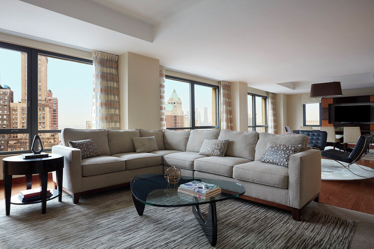 Ein modernes Wohnzimmer mit einem Ecksofa, einem Glastisch und Blick auf die Skyline durch große Fenster.